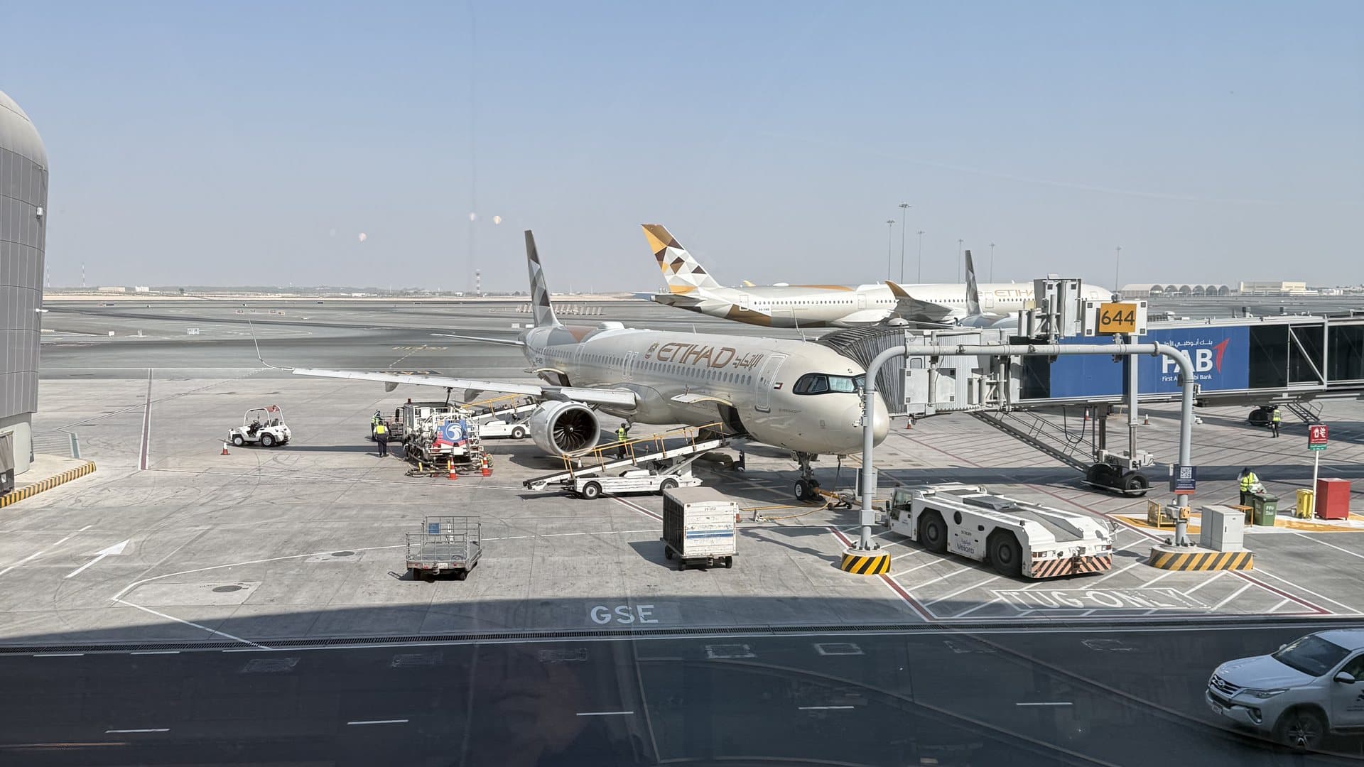 Etihad-Flugzeug am Gate in Abu Dhabi, fotografiert durch das Terminalfenster, im Hintergrund weitere Etihad-Maschinen