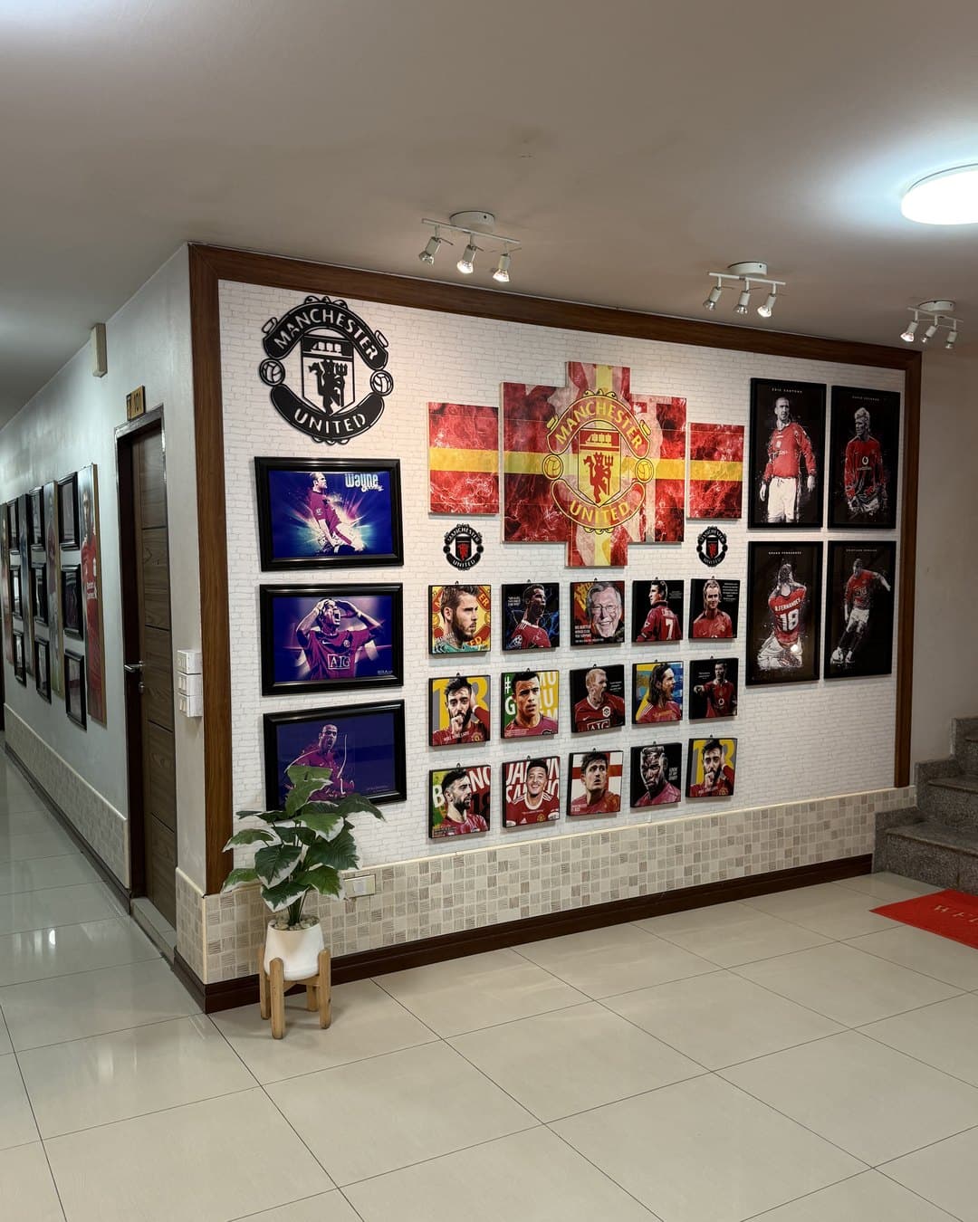 Fan-Wand mit Manchester-United-Wappen und vielen gerahmten Spielerbildern neben der Treppe im MAN.U. Hotel in Chaiyaphum