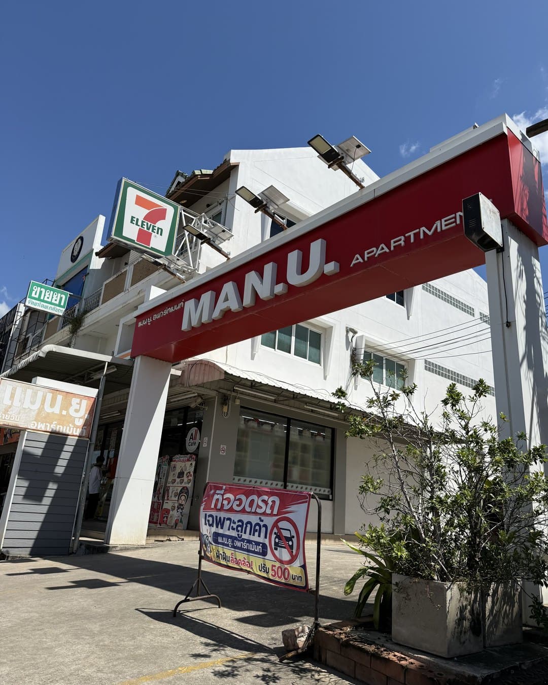 Entrance with the red MAN.U. Apartment sign, a 7-Eleven right next to it
