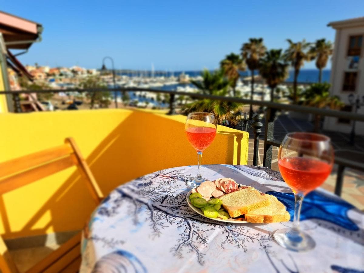Terrace at Follow the Sun with two glasses of rosé wine and a view over Portoscuso harbour to the sea