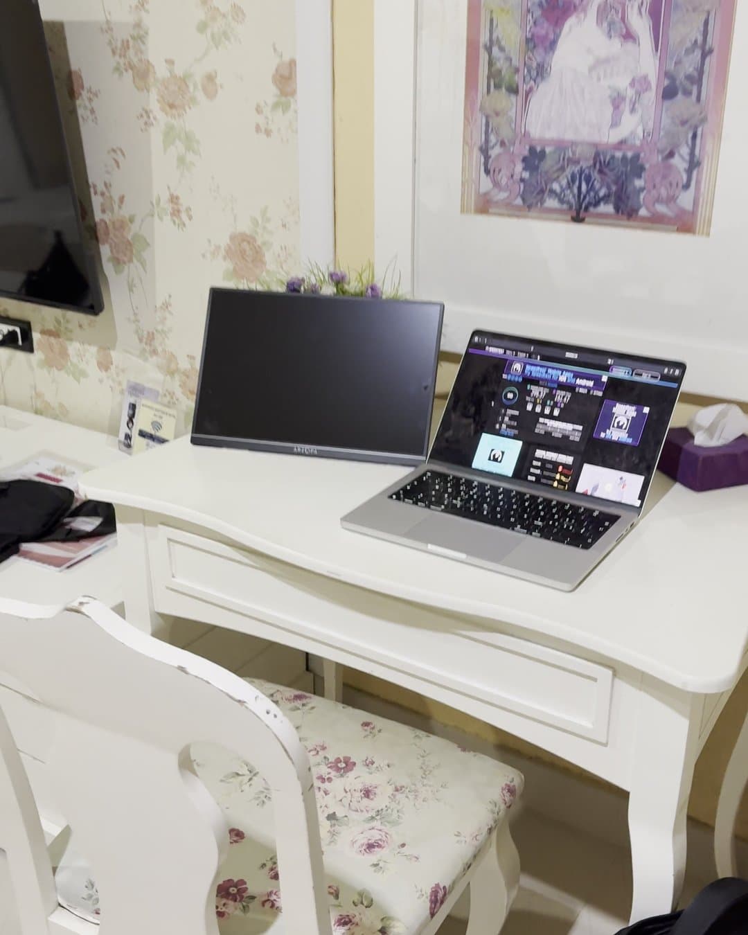 White desk with a laptop and a portable monitor, a chair with a floral cushion in front