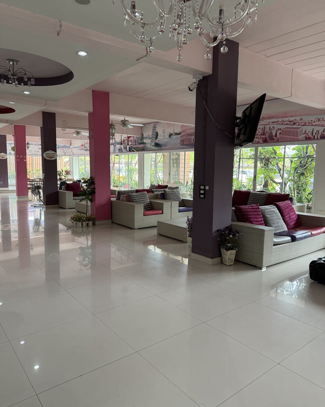 Large lobby with a light tiled floor, a chandelier, pink pillars and sofas with pink cushions